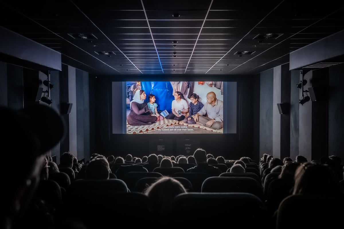 Na zdjęciu ludzie siedzący w kinie, w tle kolorowy ekran - grafika artykułu